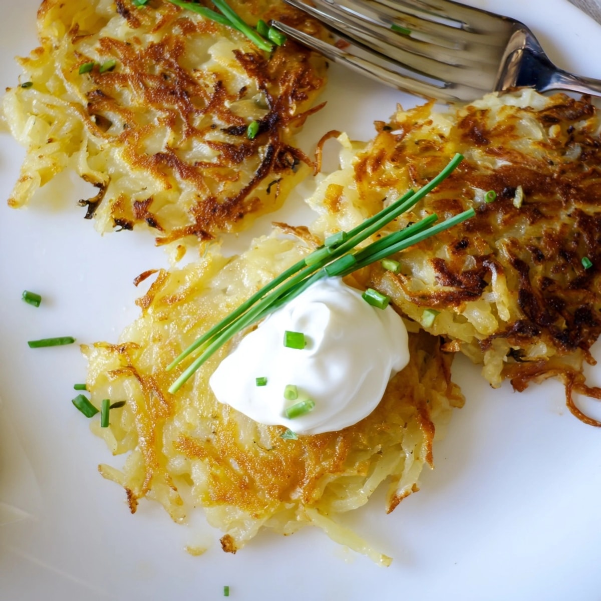 Nahaufnahme von frisch zubereiteten Kartoffelpuffern, serviert mit Sauerrahm und gehacktem Schnittlauch.