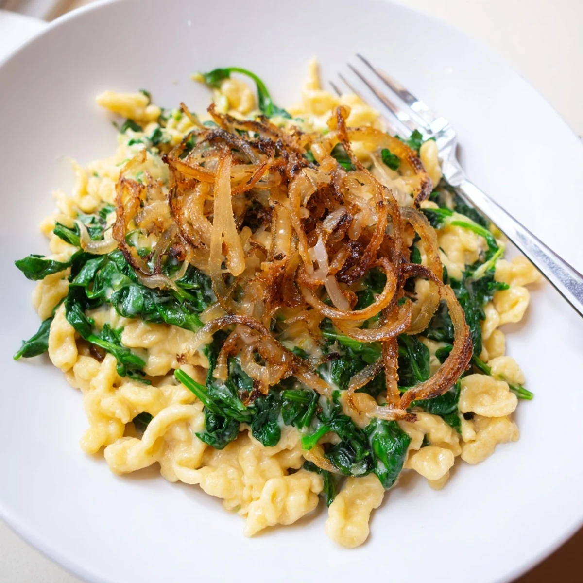 Zarte Spätzle mit Spinat und Käse, gekrönt mit knusprigen Zwiebeln für ein herzhaftes Gericht.  