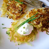 Nahaufnahme von frisch zubereiteten Kartoffelpuffern, serviert mit Sauerrahm und gehacktem Schnittlauch.